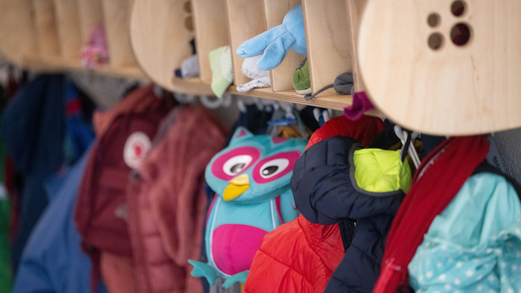 Bunte Jacken und Taschen hängen an einer Garderobe einer Kita.