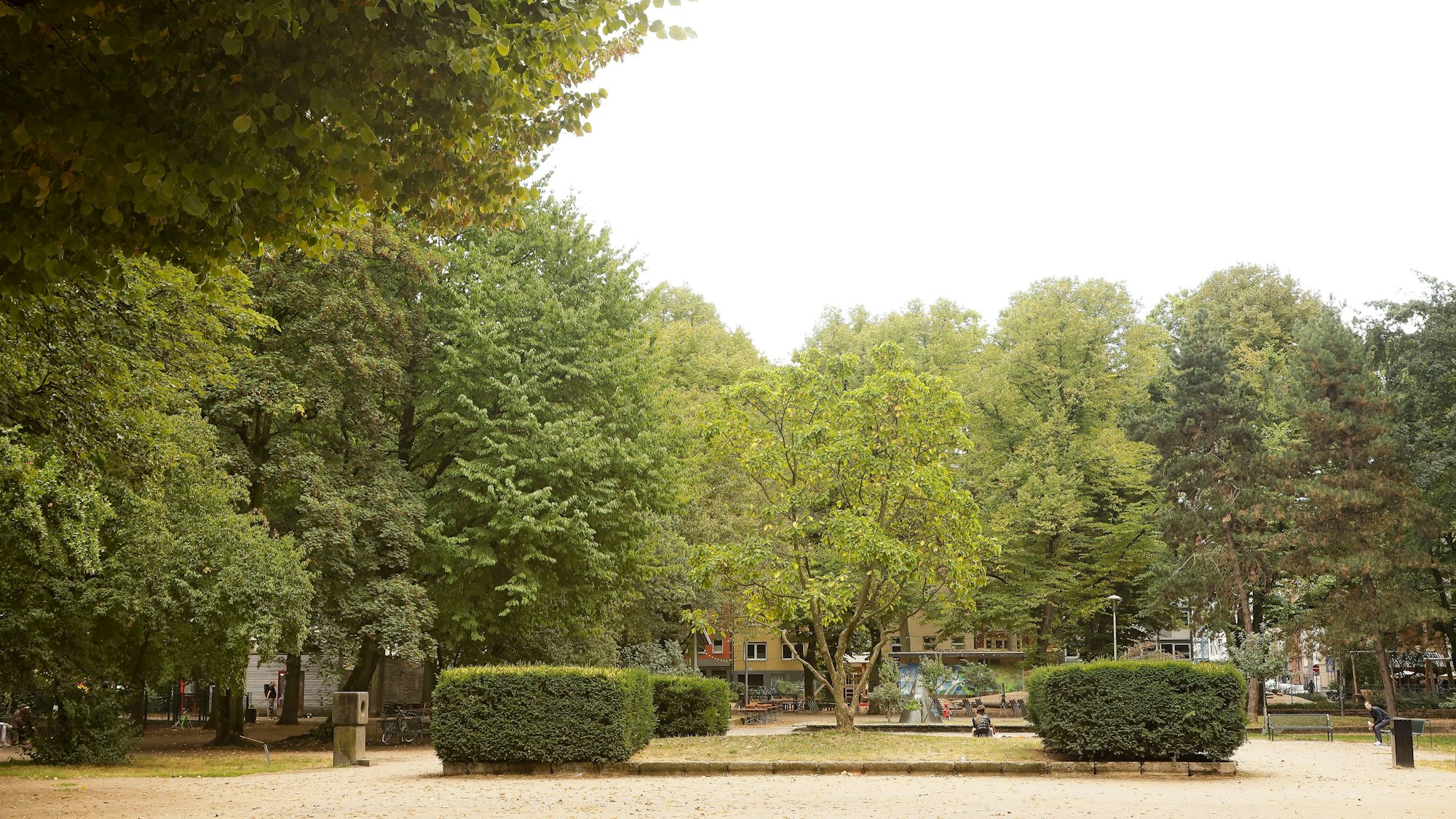 Ein von grünen Bäumen und Hecken umstandener Platz ist zu sehen.