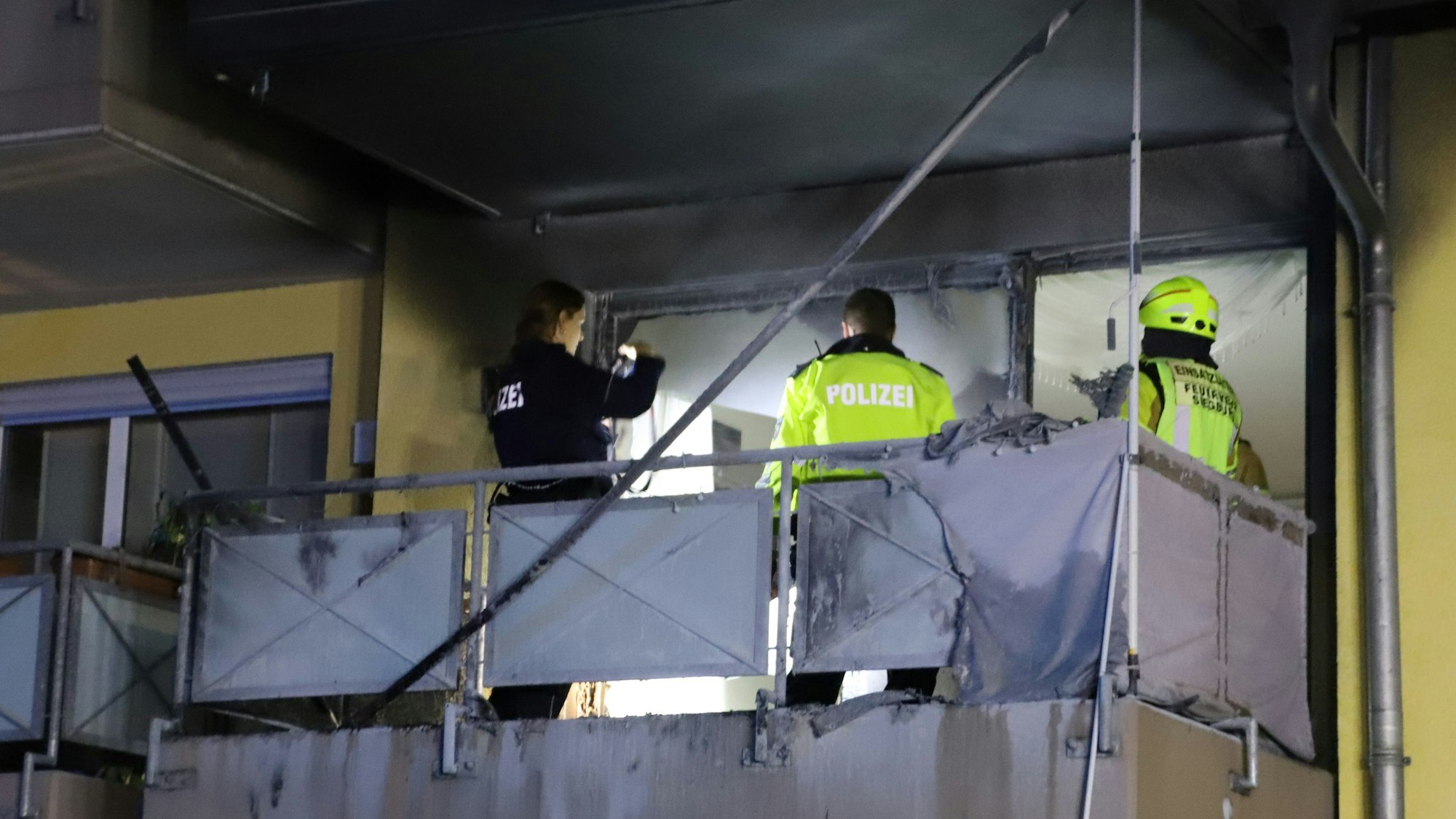 Einsatzkräfte der Polizei stehen auf dem Balkon und untersuchen den Brandherd.