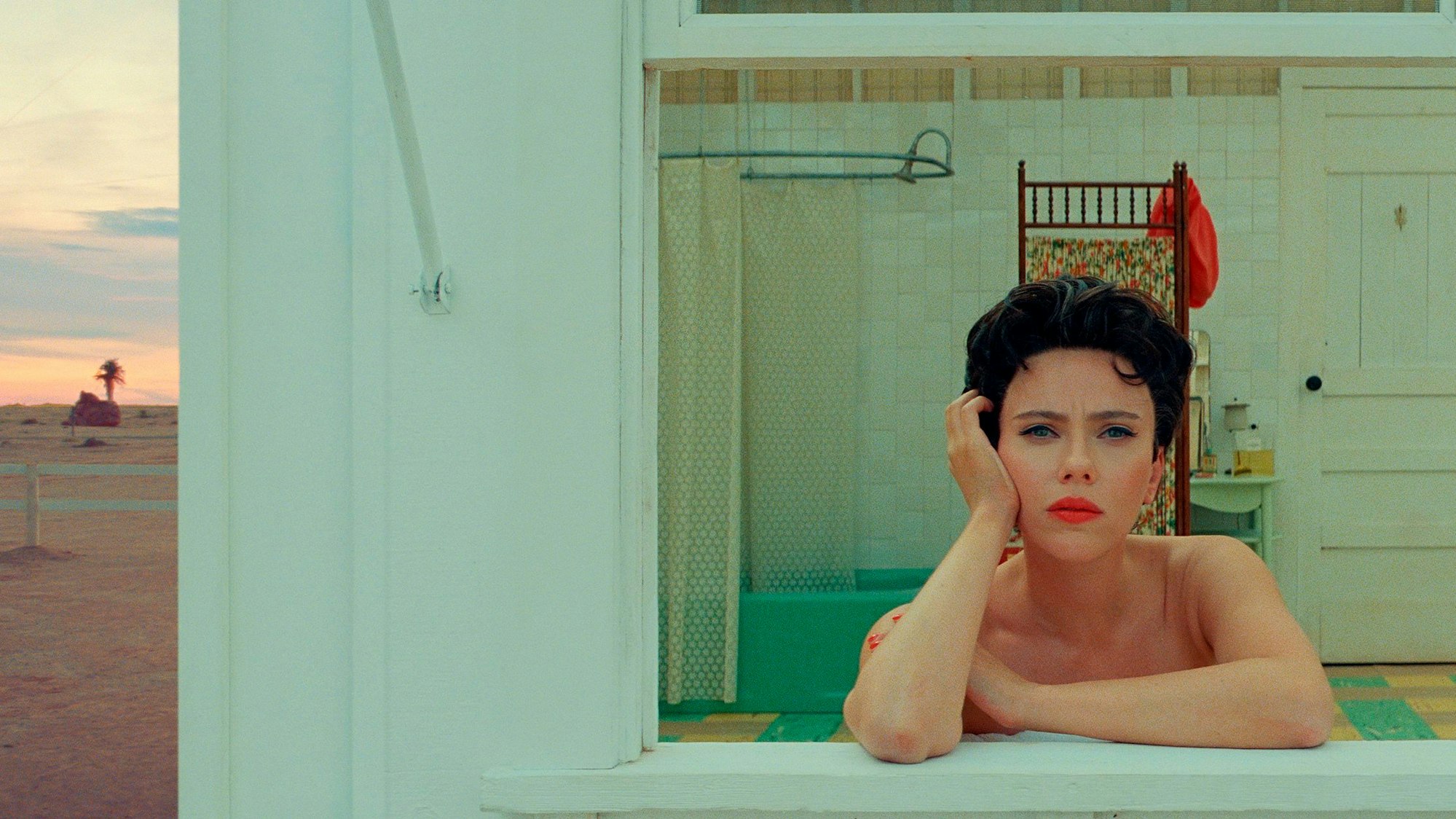 Scarlett Johansson in einer Szene aus „Asteroid City“. Sie schaut mit trauriger Miene aus dem Fenster eines Holzhauses.