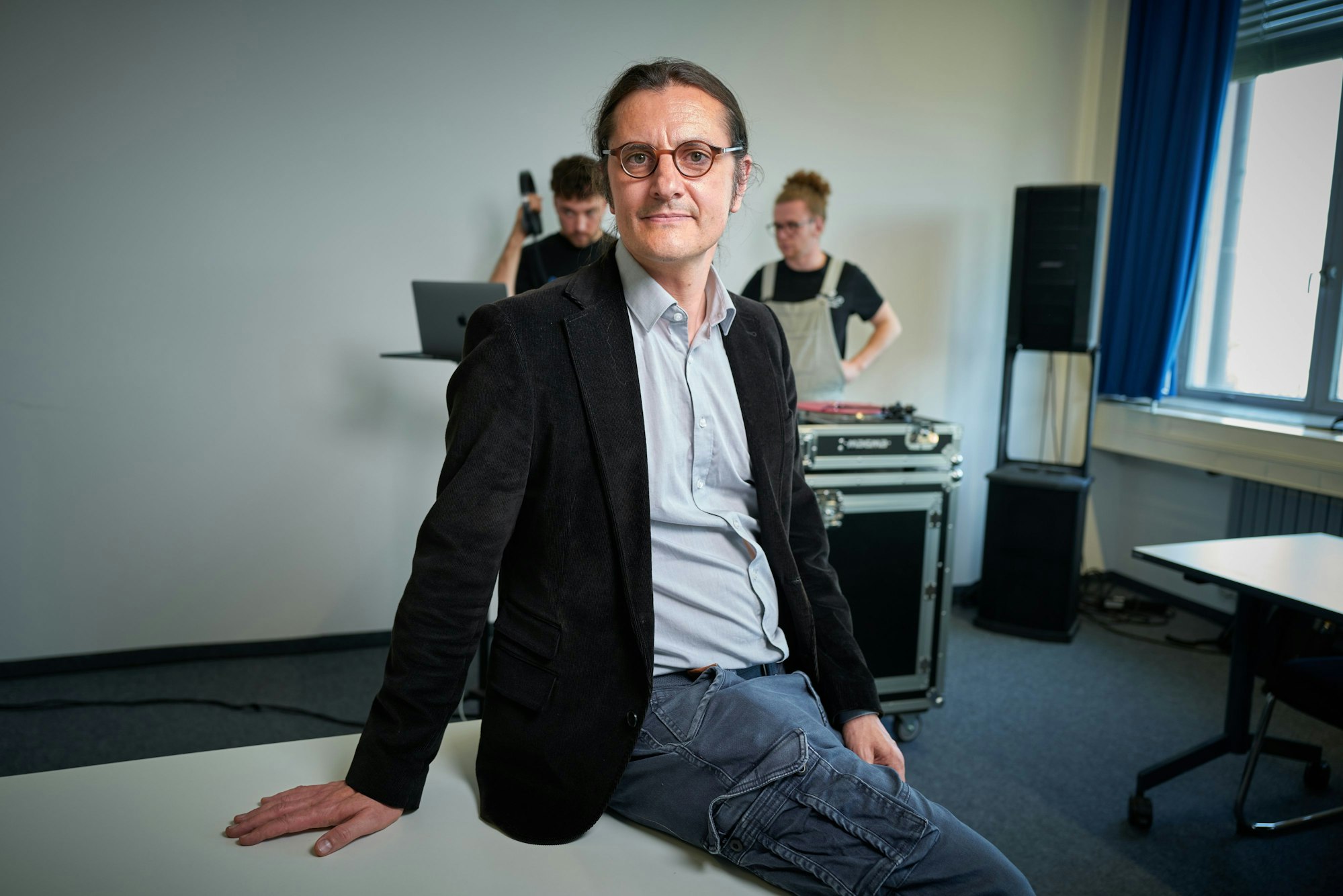 Professor Oliver Kautny lehnt an einer Tischkante und schaut in die Kamera.