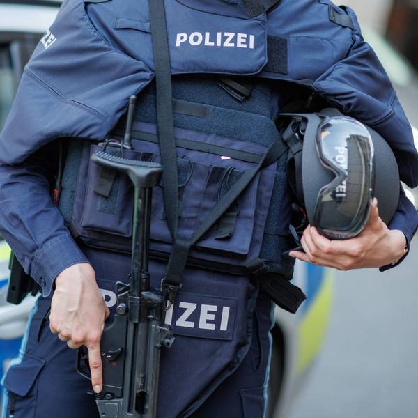Eine Polizistin steht mit ballistischem Schutzhelm, einer Schusswaffe und einer kugelsicheren Weste vor einem Polizeiwagen.