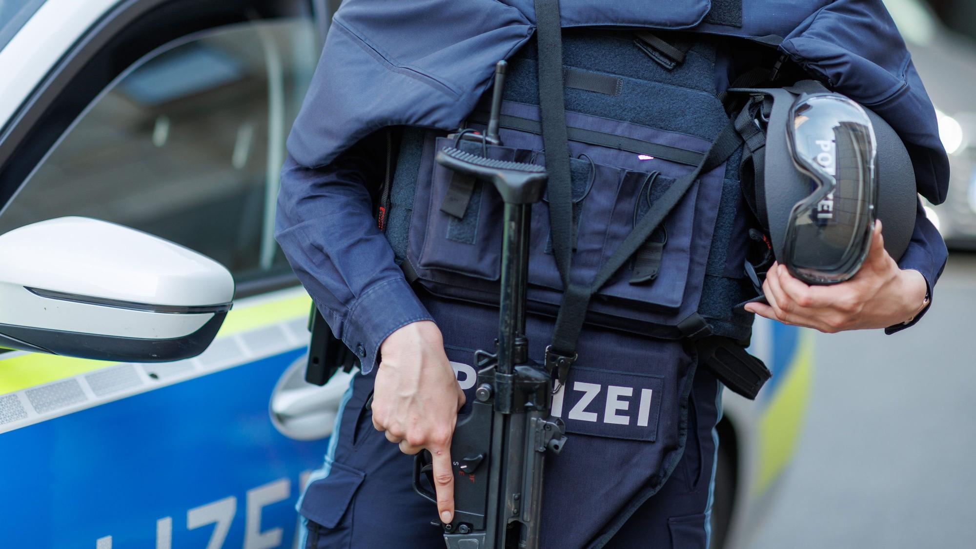 Eine Polizistin steht mit ballistischem Schutzhelm, einer Schusswaffe und einer kugelsicheren Weste vor einem Polizeiwagen.