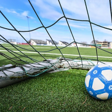Ein Fußball liegt in einem Tor, das auf einem leeren Fußballplatz steht.