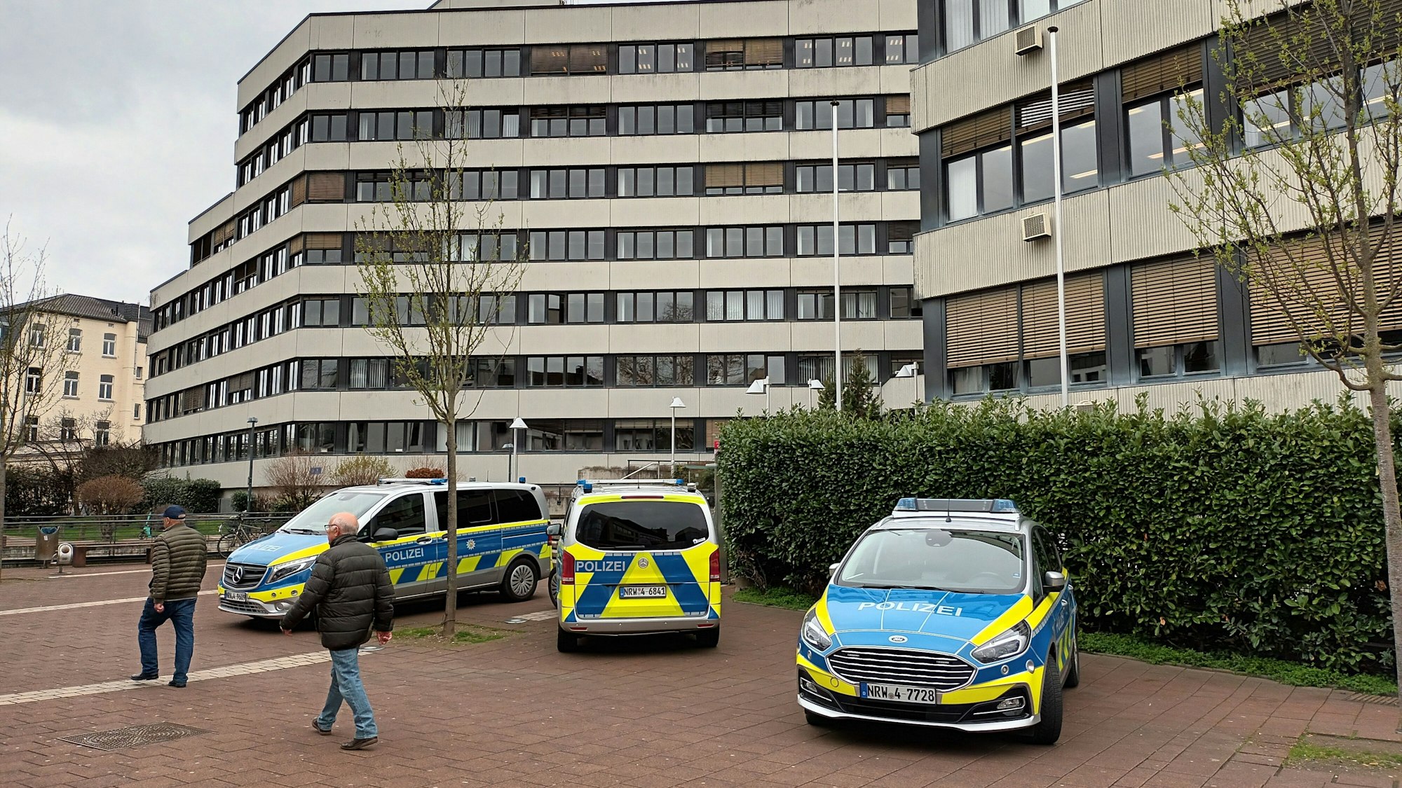 Vor dem Amtsgericht Siegburg stehen drei Poilizeiwagen. Zwei Personen laufen daran vorbei.