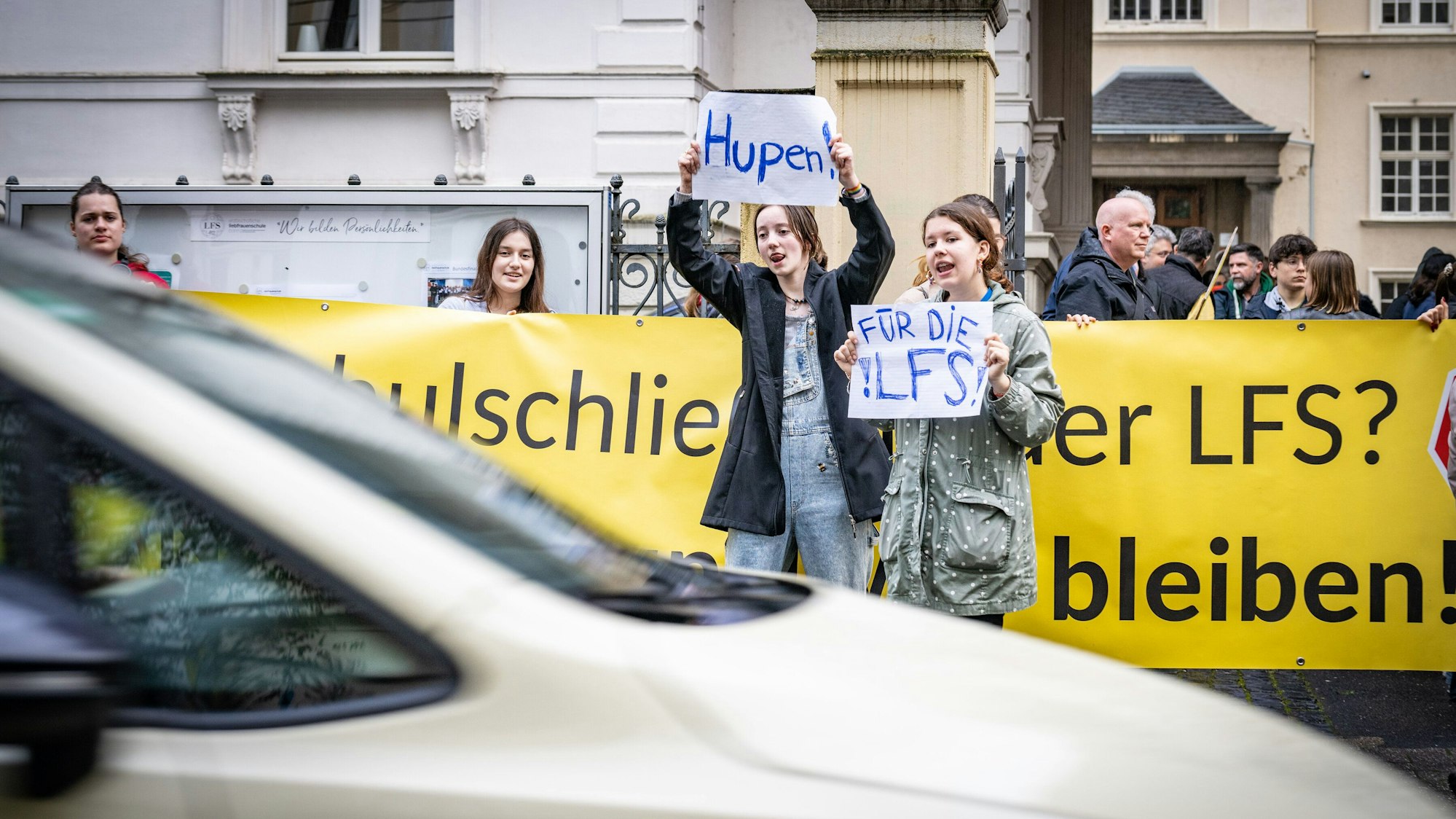 Mädchen halten Schilder in die Luft, auf denen „Hupen für die LFS“ steht.