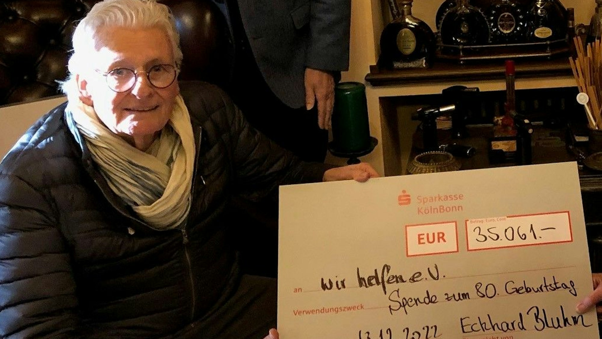 Der Kölner Textilunternehmer Eckhard Bluhm hält einen großen, symbolischen Scheck über 35.061 Euro in der Hand.