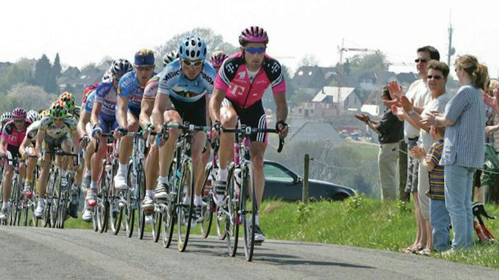 Radsportler fahren die Streckenpassage bei Heiligenhaus. Zuschauende applaudieren vom Streckenrand aus.