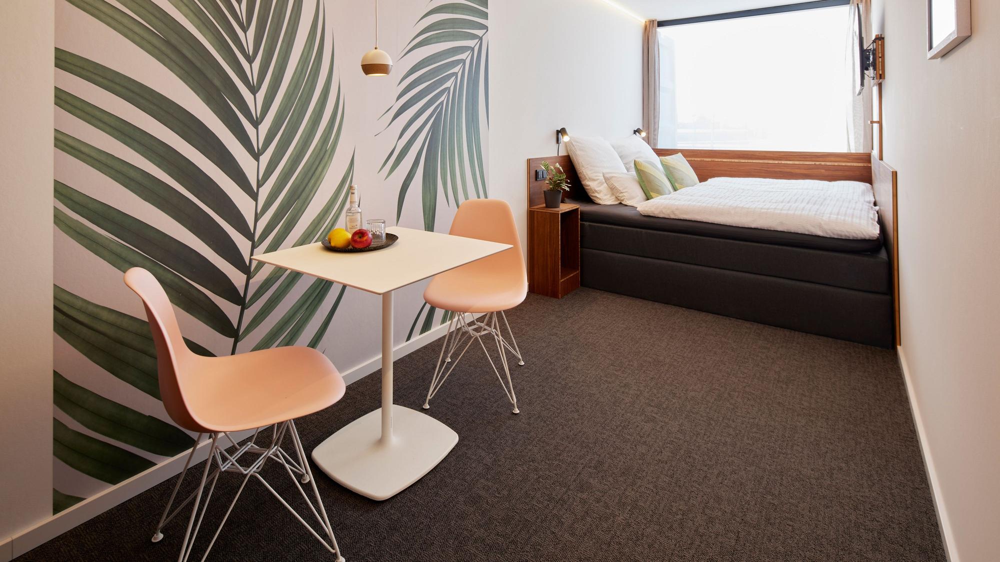 Am Ende des Raums steht ein Bett, im Vordergrund steht ein Tisch mit Stühlen.