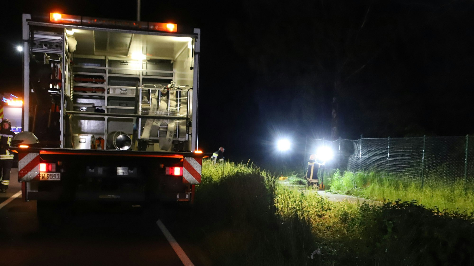 Die Feuerwehr leuchtet die Unfallstelle aus. Im Vordergrund der Einsatzwagen. Daneben der Grünstreifen.