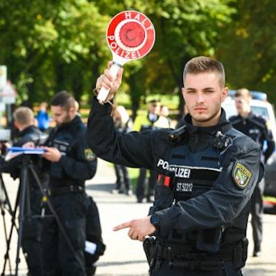 Mit einer Haltekelle winkt ein Polizist Autofahrer aus dem Verkehr.