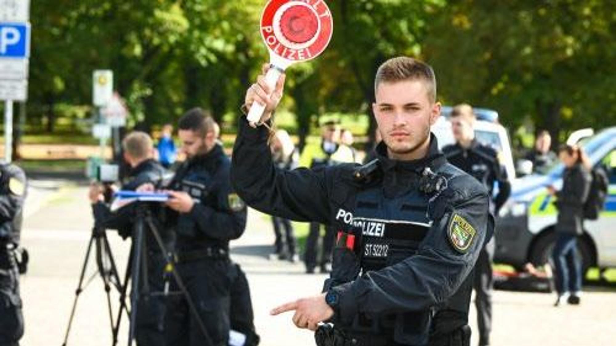 Mit einer Haltekelle winkt ein Polizist Autofahrer aus dem Verkehr.