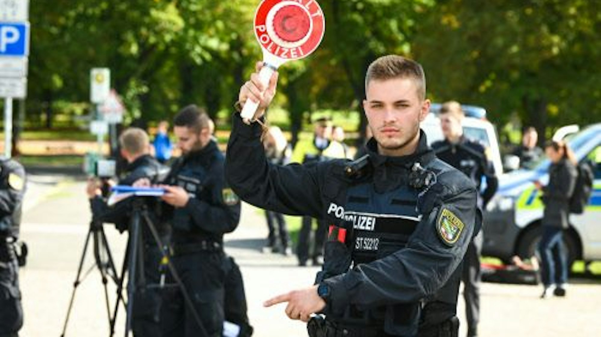 Mit einer Haltekelle winkt ein Polizist Autofahrer aus dem Verkehr.