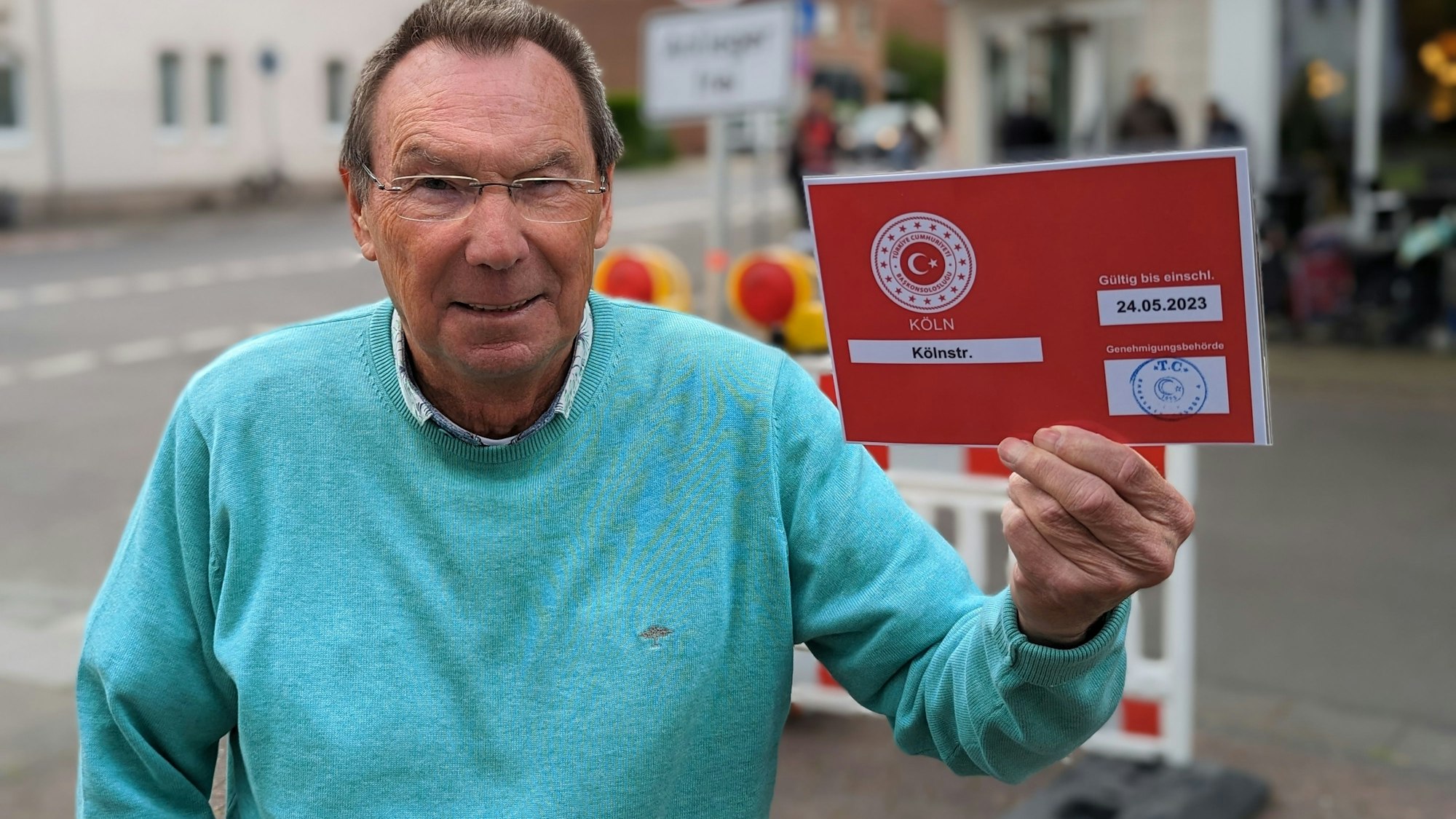 Auf dem Foto ist Jürgen Wiedenau zu sehen. Er hält die rote Durchfahrtsgenehmigung vom Konsulat, die er in seinem Briefkasten gefunden hat, in seiner Hand.