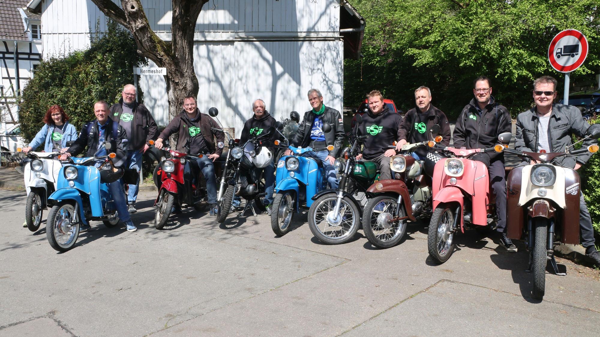 Mehrere Männer und eine Frau stehen mit ihren Simson-Mopeds in einer Reihe.