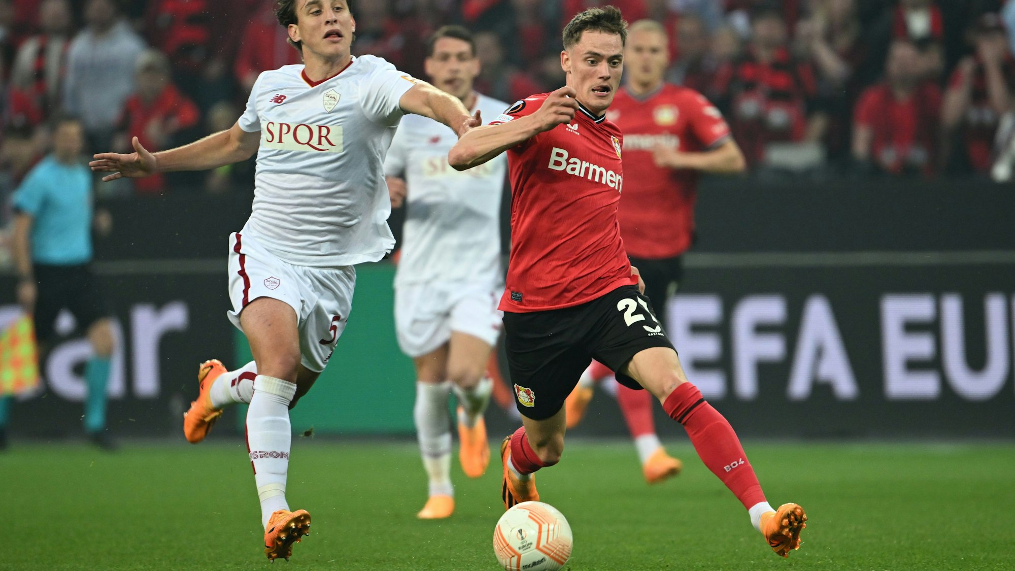 Roms Edoardo Bove in einem weißen Trikot (l) und Leverkusens Florian Wirtz in rot kämpfen um den Ball.