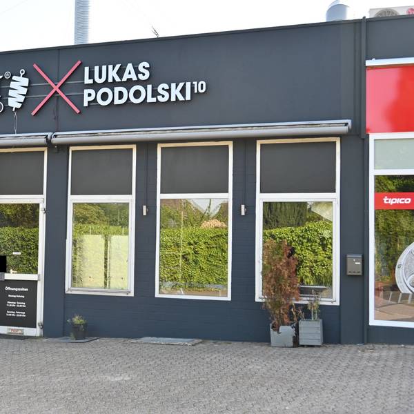 Das Bild zeigt die Filiale von Mangal-Döner in Stommeln. Auf dem dunkelgrauen Gebäude steht in großen Buchstaben "Mangal Döner" und "Lukas Podolski".