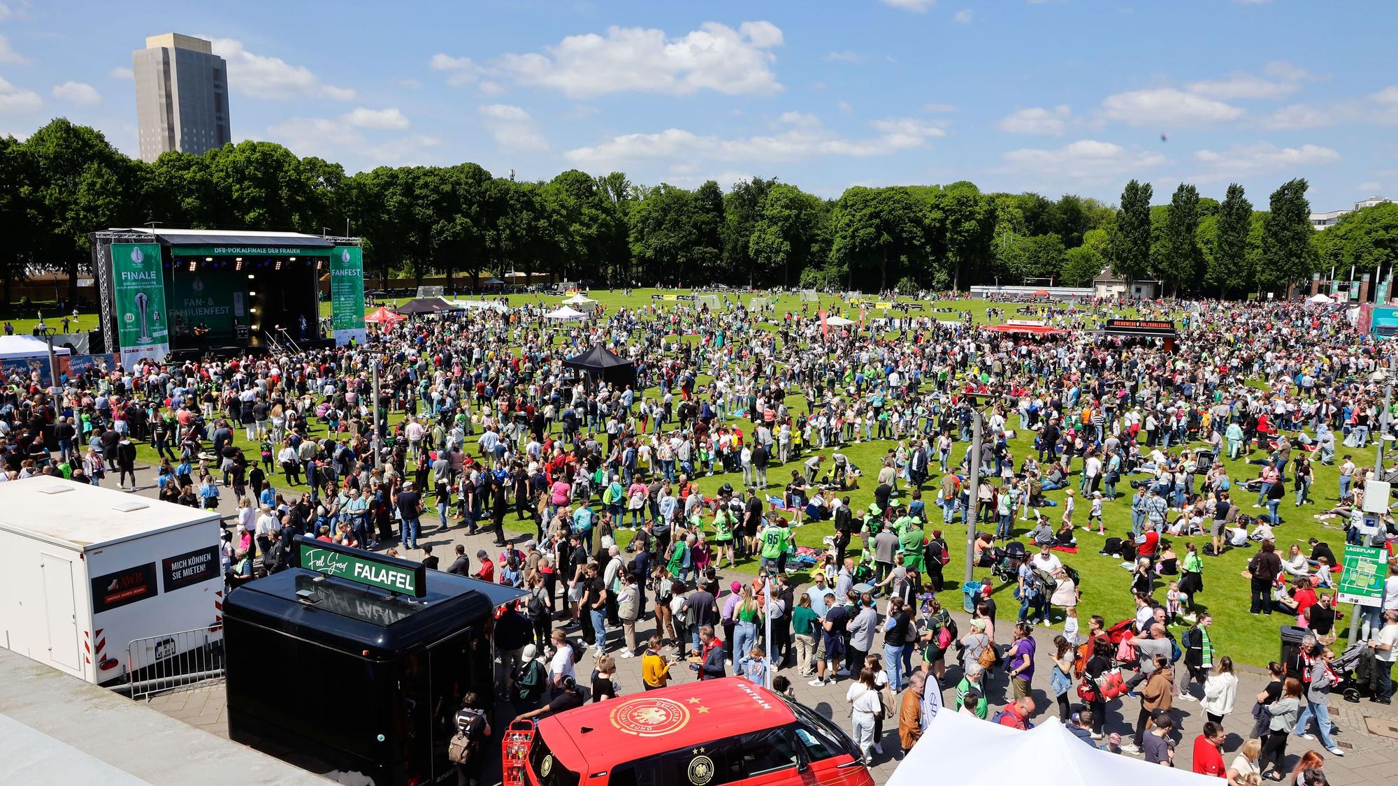 Tausende Fans stehen auf einer Wiese am Rhein-Energie-Stadion. Im Hintergrund ist eine Bühne aufgebaut.