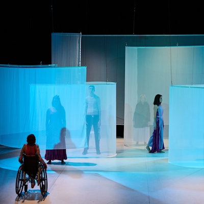 Mehrere Menschen stehen oder sitzen auf einer Theaterbühne.