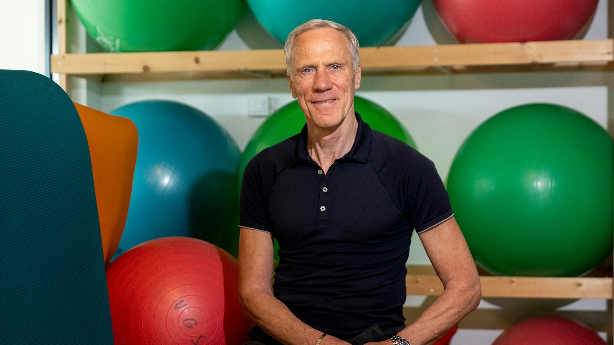 Ingo Froböse guckt in die Kamera, um ihn herum liegen Medizinbälle.