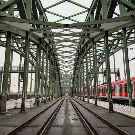 Die Gleise der Kölner Hohenzollernbrücke. Im Hintergrund ist der Kölner Dom zu sehen, rechts fährt eine S-Bahn vorbei. (Symbolbild)
