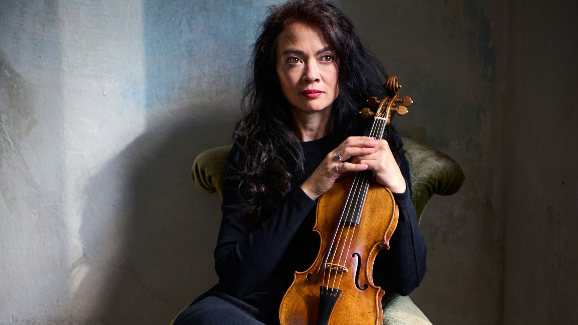 Midori Seiler sitzt mit einer Violine vor einer Wand.