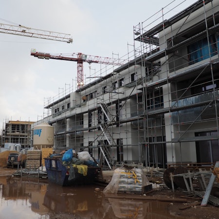 Ein Bauprojekt in Erftstadt-Konradsheim ist zu sehen. Zwei Kräne und ein dreistöckiges Haus sind Inhalt des Bildes und der Baustelle.