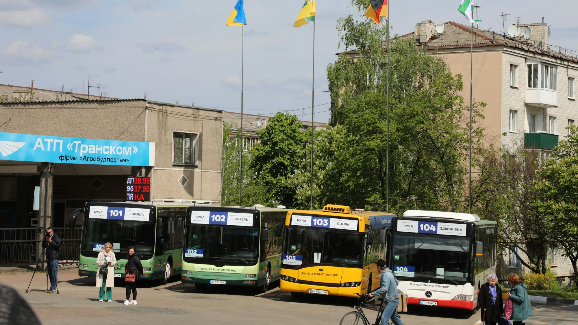 Vier Busse stehen unter Fahnen auf einem Platz.