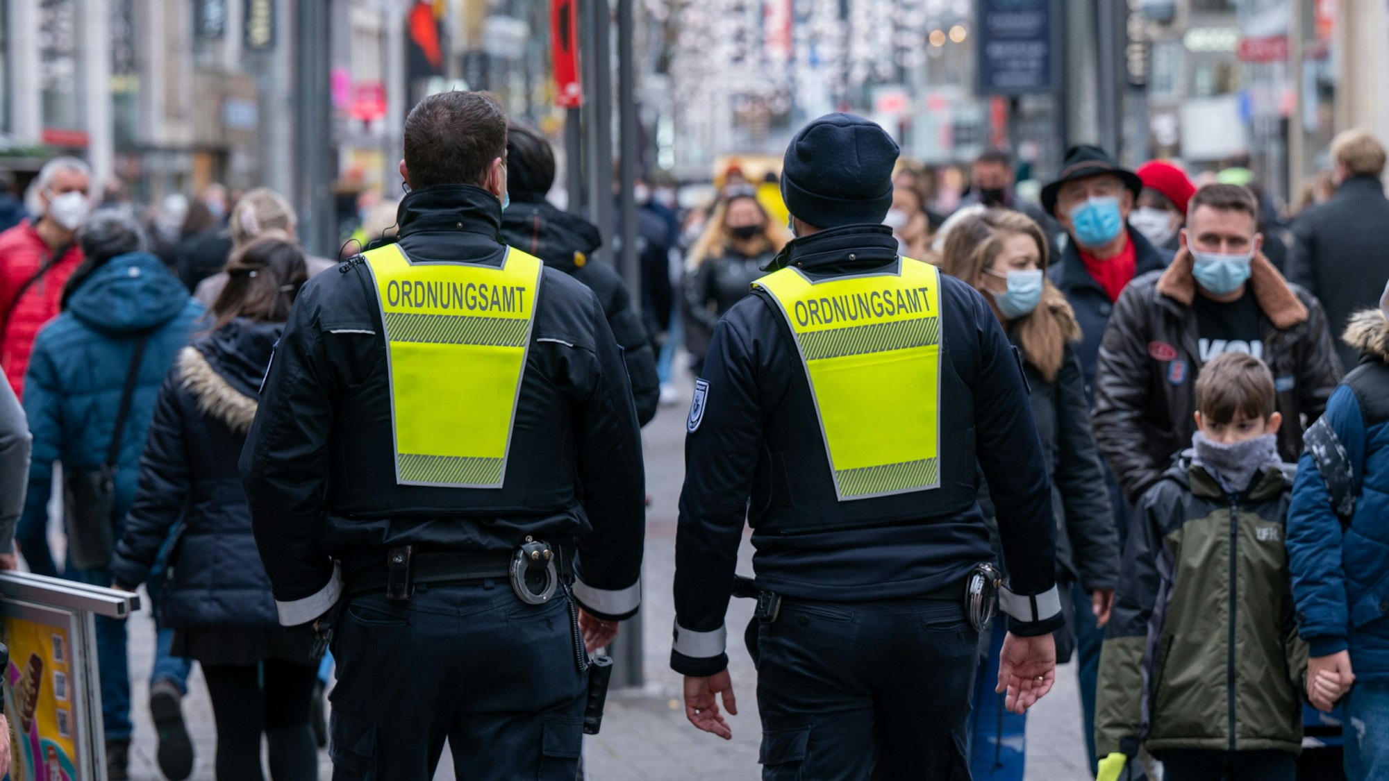 Zwei Mitarbeiter des Ordnungsamtes erinnern Passanten an die Maskenpflicht.