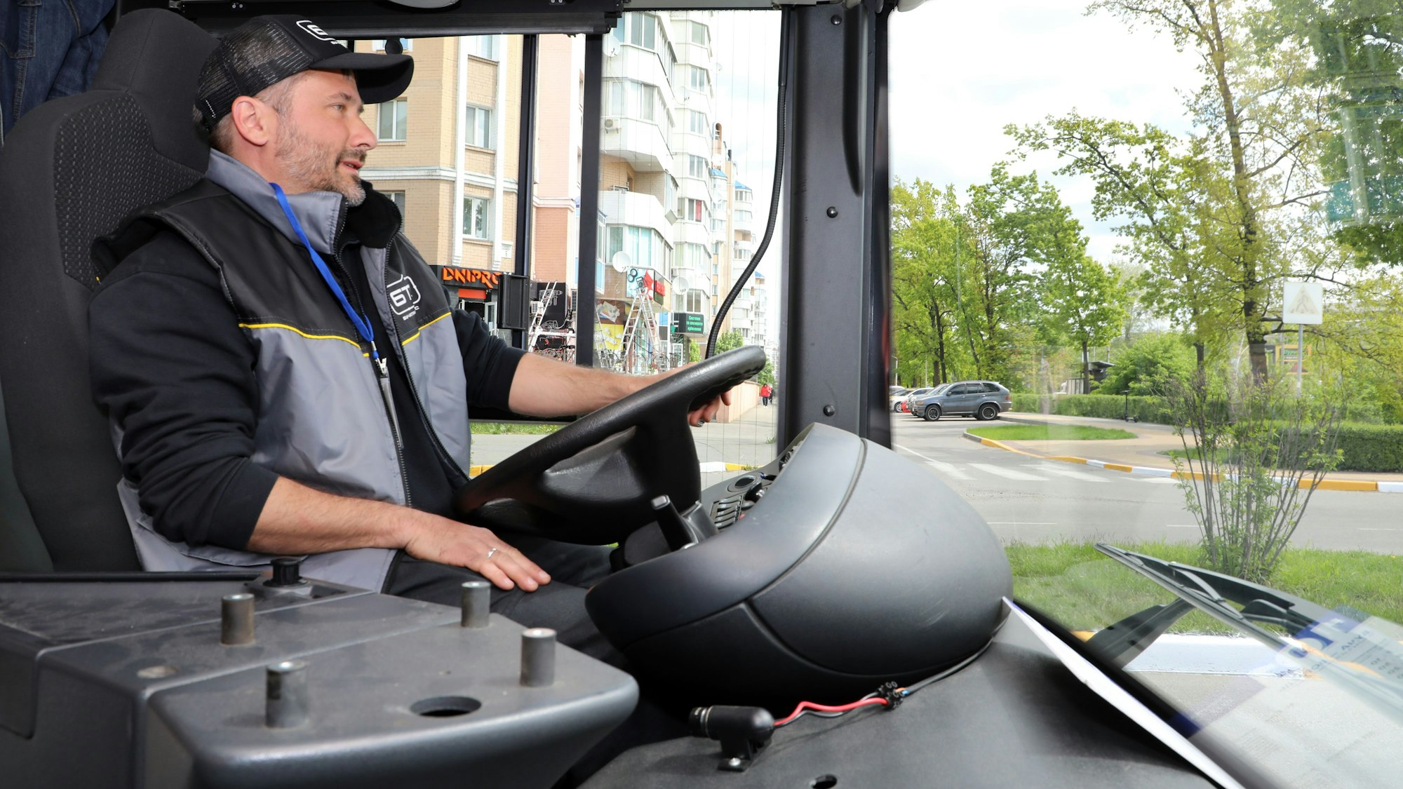 Ein Mann sitzt mit Käppi und Weste am Steuer eines Linienbusses in Butscha.
