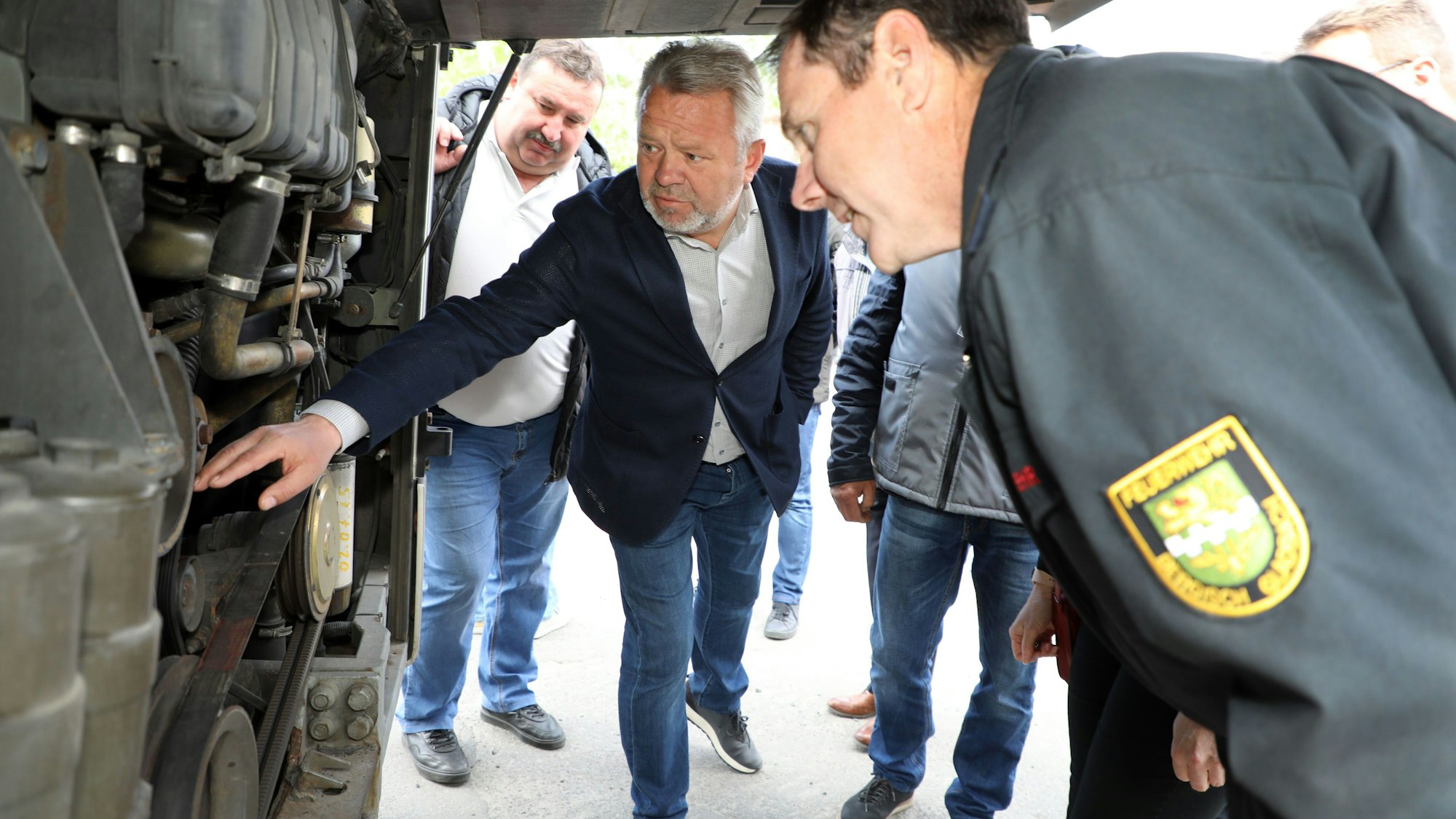 Zwei Männer schauen in den Motorraum eines Busses.