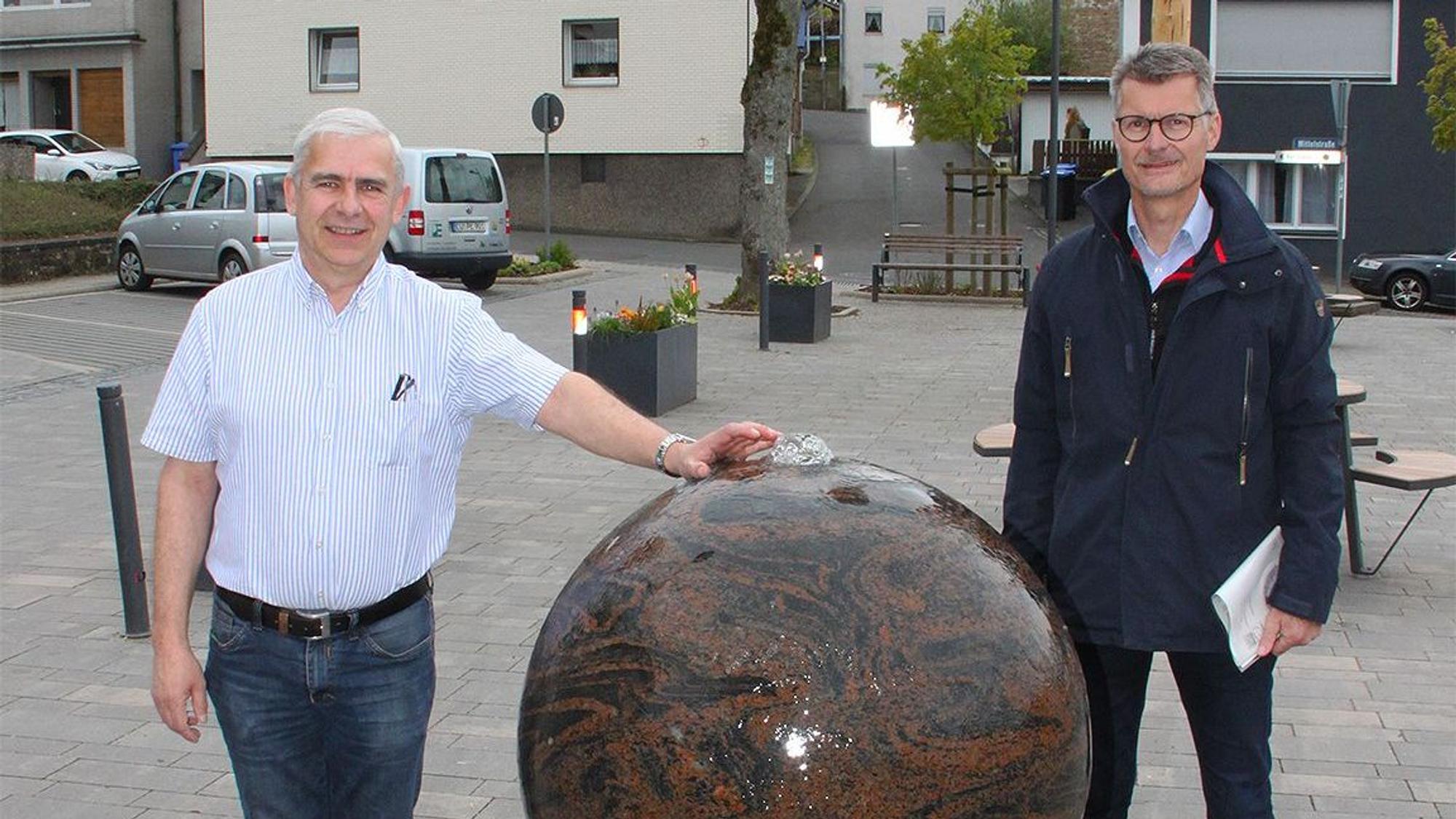 Es sind die beiden Männer mit dem Kugelbrunnen zu sehen.