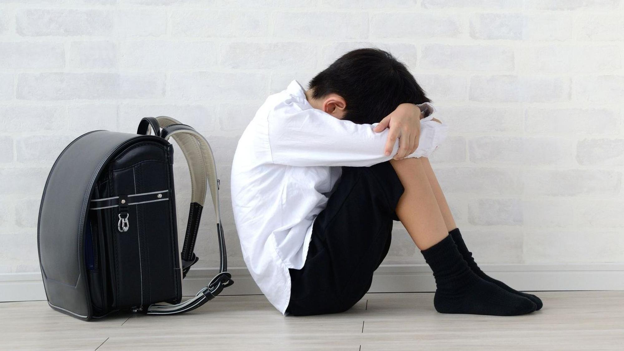 Ein Schuljunge sitzt vor seinem Schulranzen und hält seinen Kopf zwischen den Armen