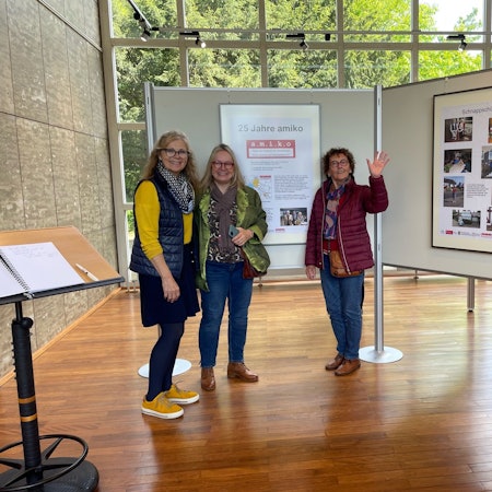 Drei Frauen stehen vor einer Ausstellungstafel.