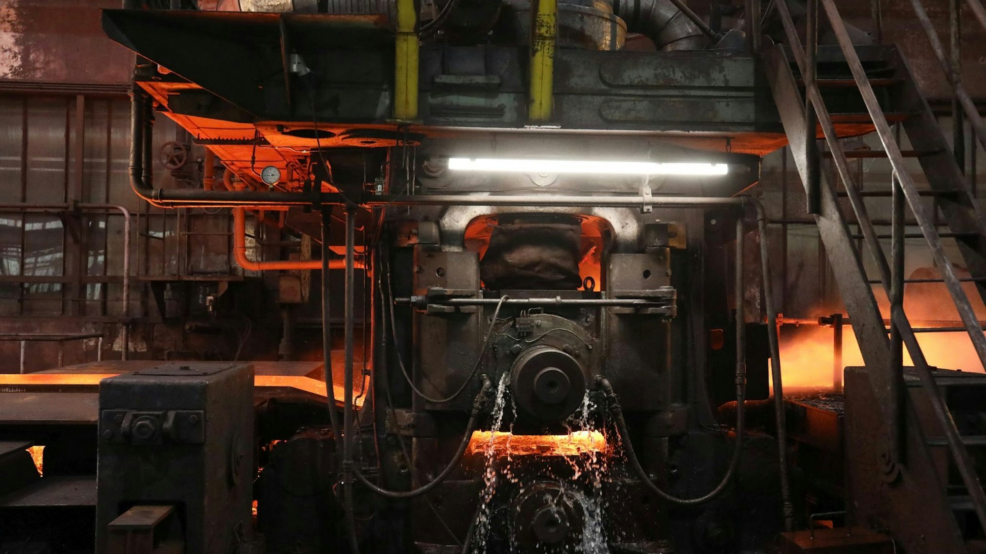 In einer schweren Maschine wird rot glühender Stahl zu Breitfachstahl gepresst;