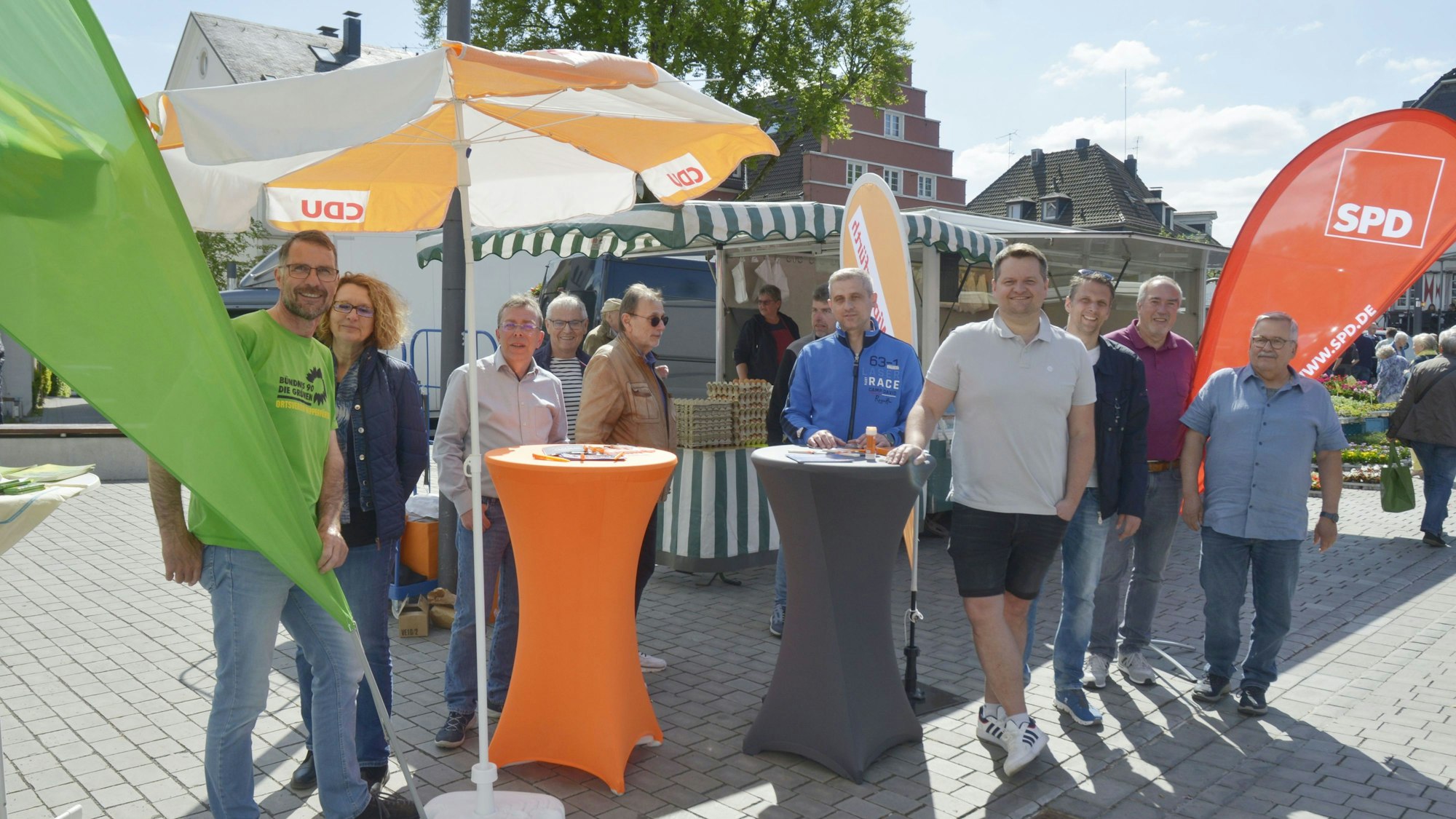 Es sind mehrere Mitglieder der drei Parteien zu sehen, wie sie vor ihren ständen stehen.