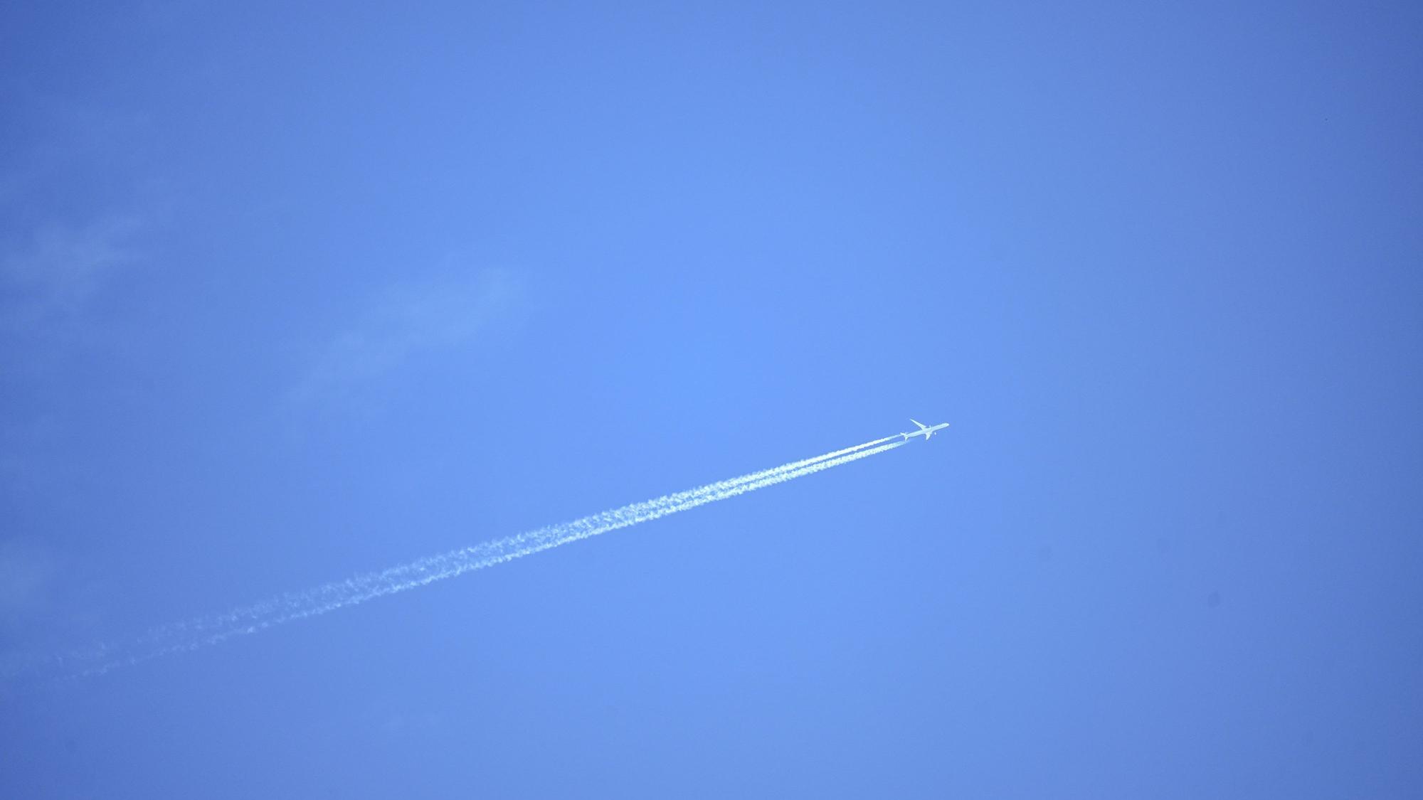 Ein Flugzeug zieht Kondensstreifen in den blauen Himmel.