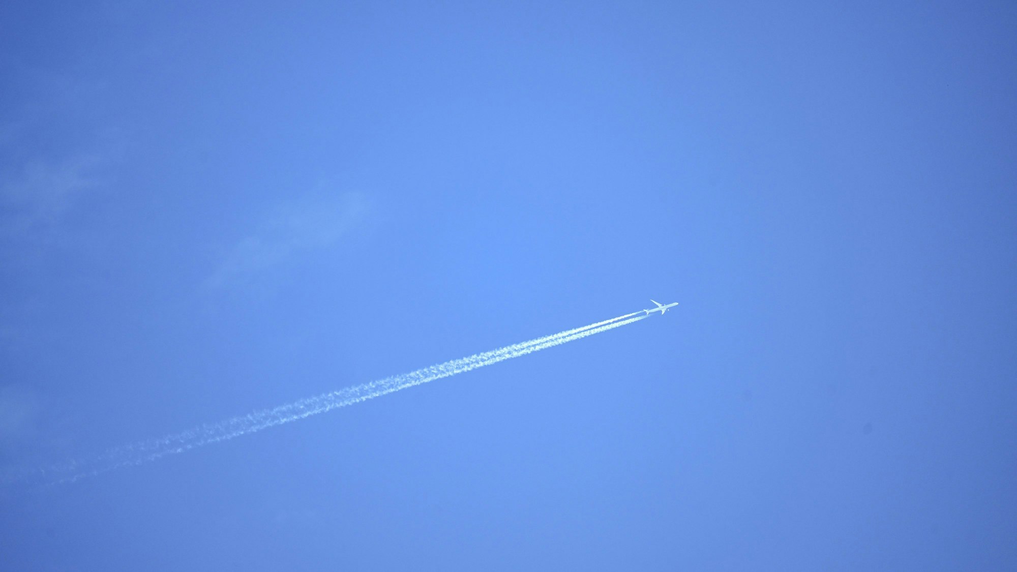 Ein Flugzeug zieht Kondensstreifen in den blauen Himmel.