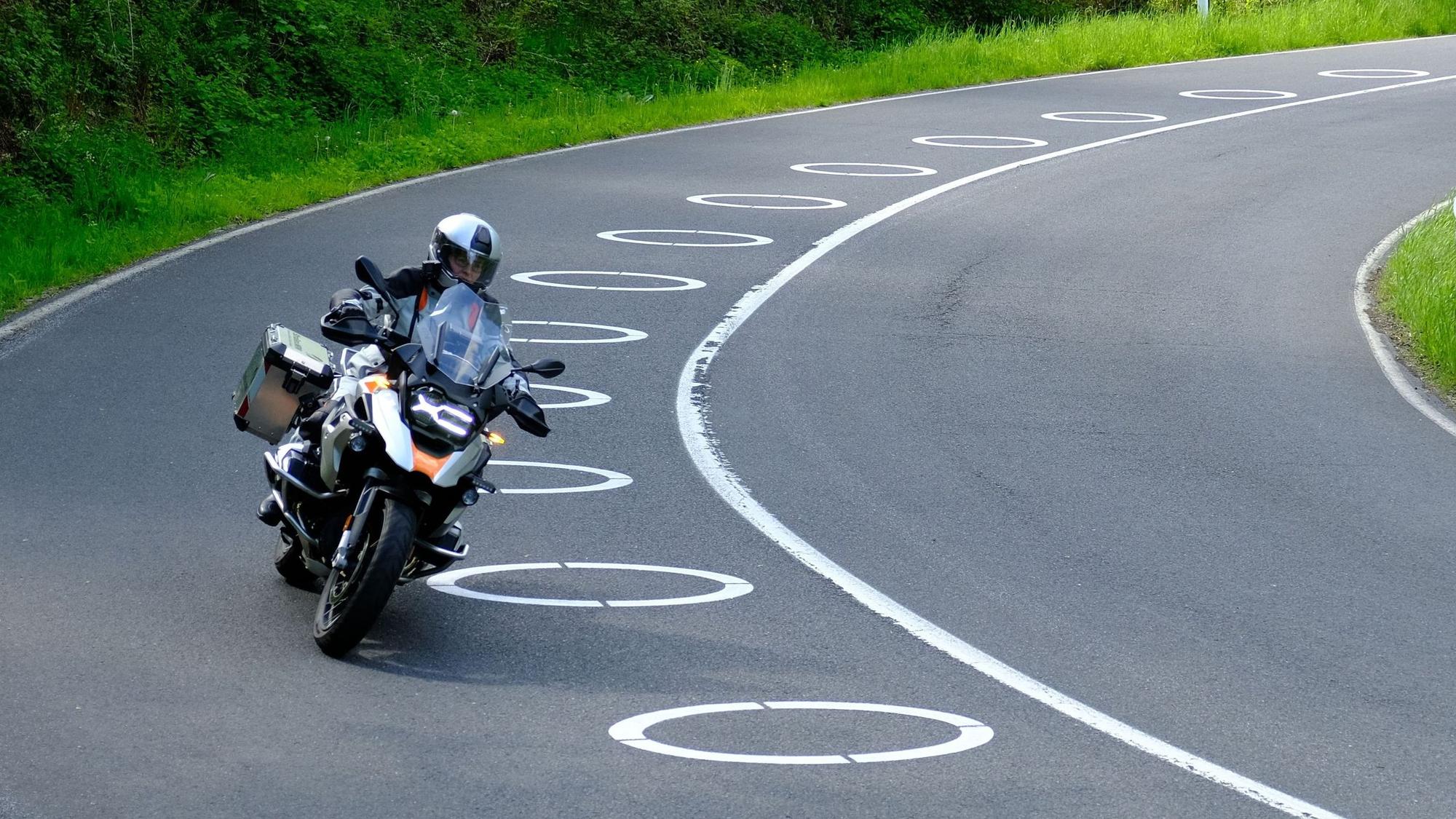 Ein Motorradfahrer umfährt mit einem Bike in einer Linkskurve auf der Fahrbahn angebrachte, ellipsenförmige Fahrbahnmarkierungen.