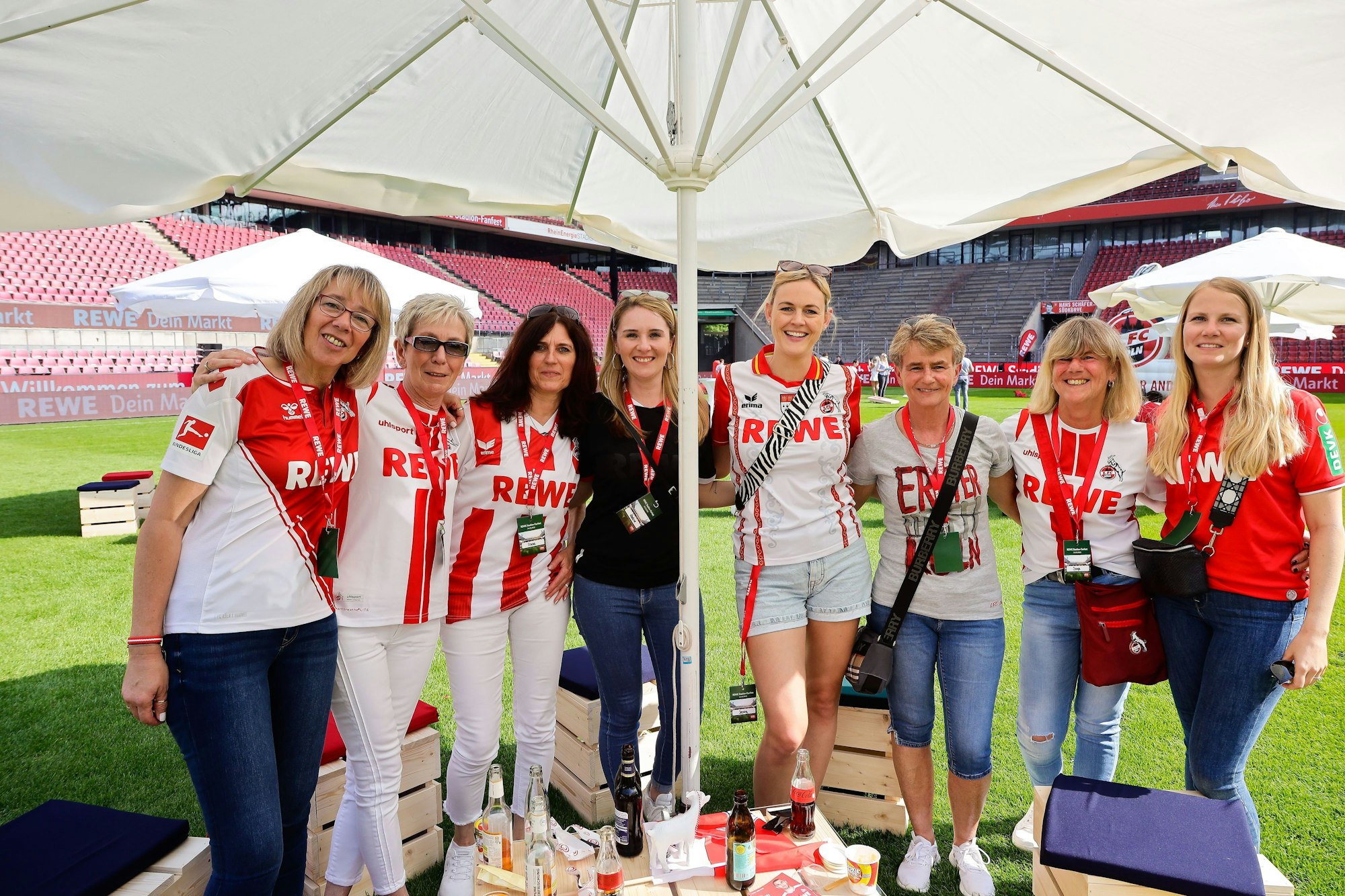 Frauen mit Fan-Trikots stehen unter einem Sonnenschirm im Stadion.