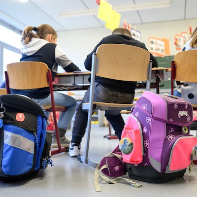 Kinder sitzen mit ihren Ranzen in einer Klasse.