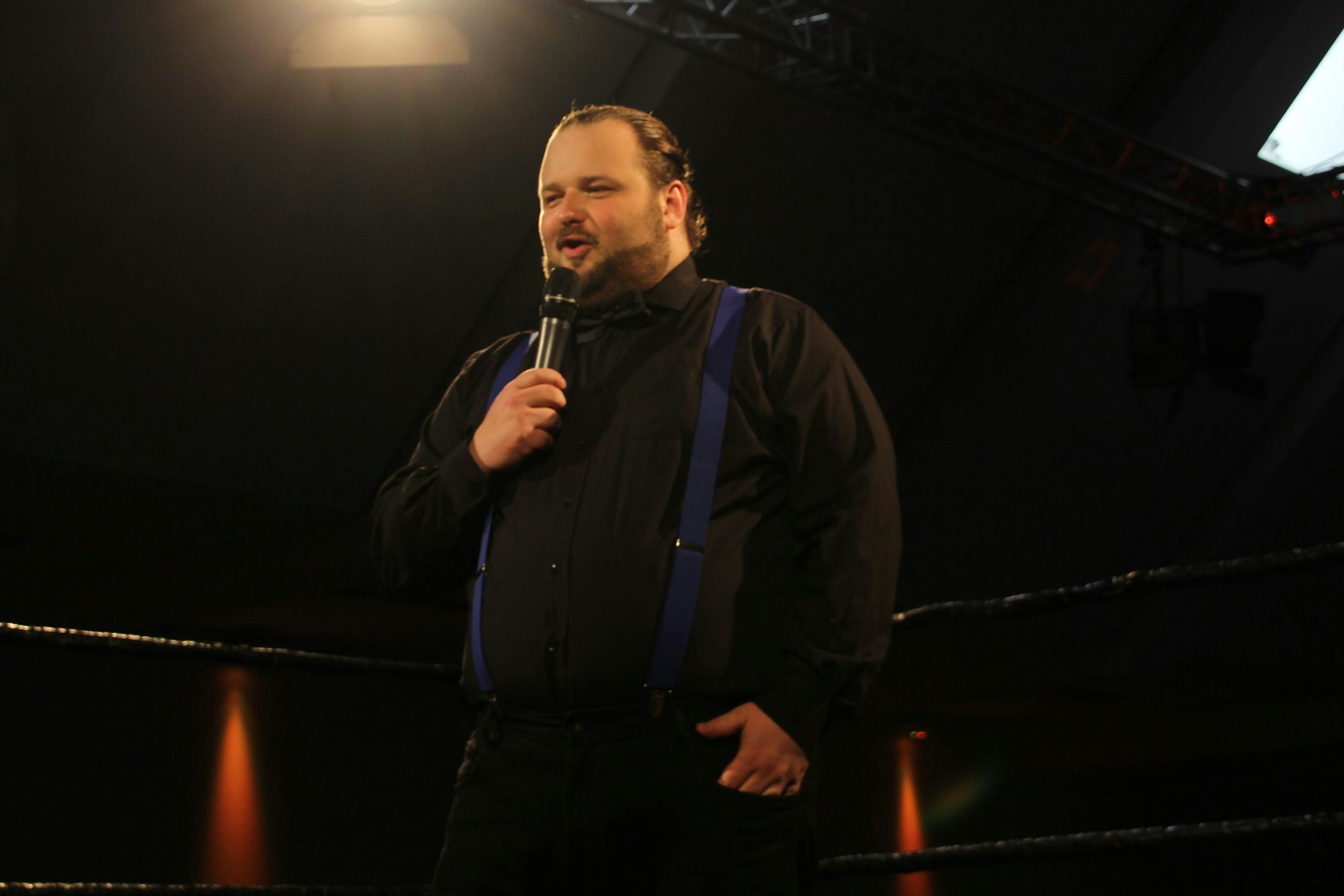 In einem Ring steht Andreas Wendl mit einem Mikrofon in der Hand und spricht zum Publikum.