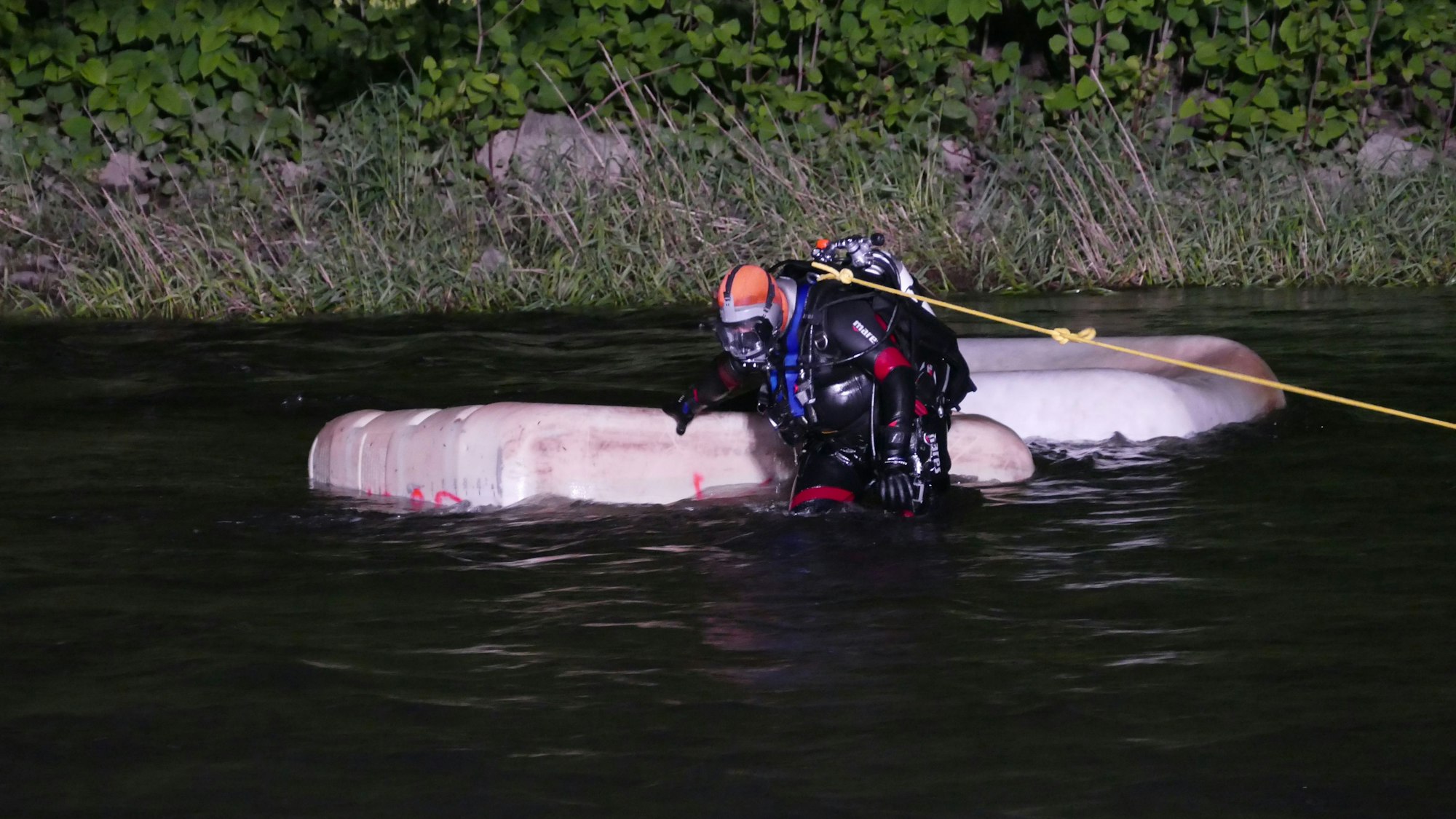 Ein Bergungstaucher befindet sich an einer Leine im Wasser neben zwei Tanks.