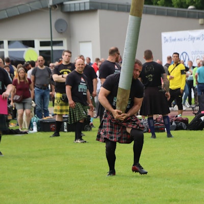 Das Bild zeigt einen Mann im Kilt, der einen Baumstamm in die Höhe hievt.