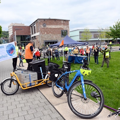 Zu sehen sind in gelbe Westen gekleidete Radfahrer, die sich versammeln und Transparente hochhalten.