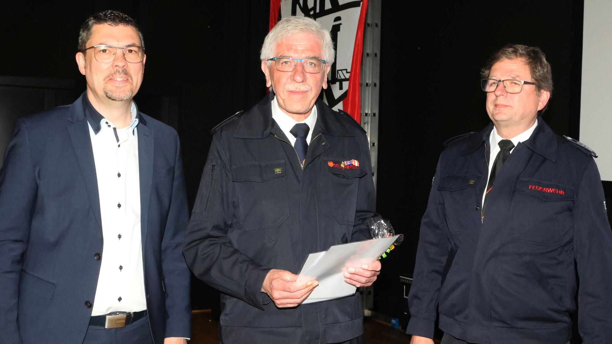 Im Bild sind zwei Feuerwehrmänner und ein Bürgermeister zu sehen.