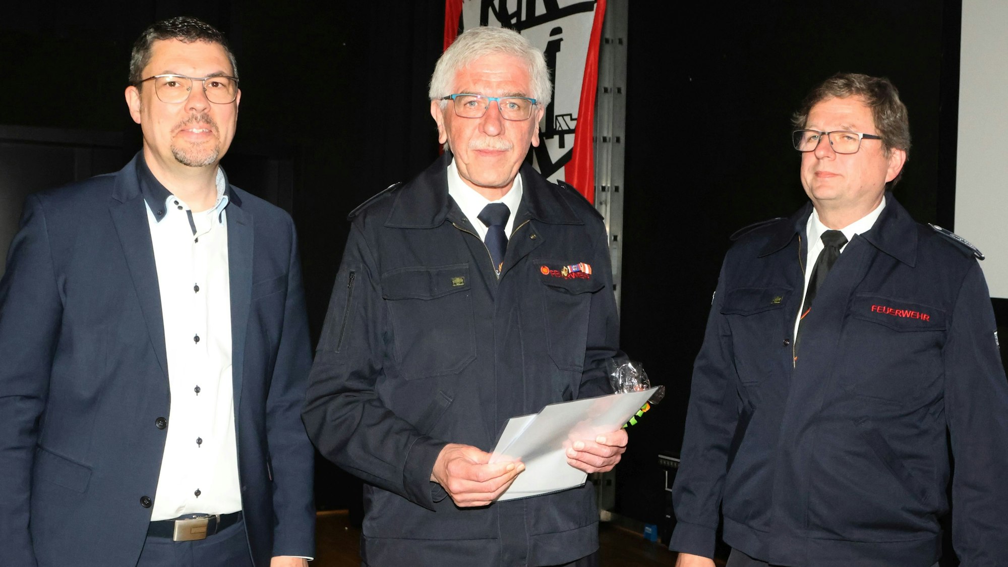 Im Bild sind zwei Feuerwehrmänner und ein Bürgermeister zu sehen.