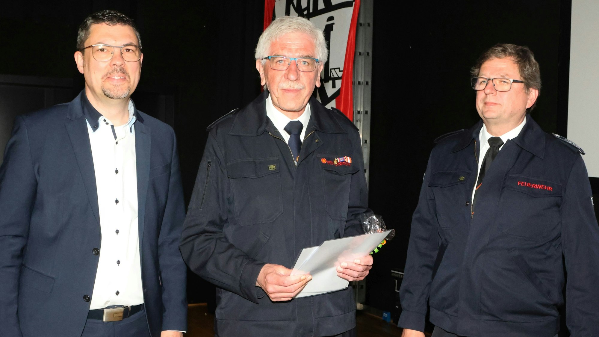 Im Bild sind zwei Feuerwehrmänner und ein Bürgermeister zu sehen.