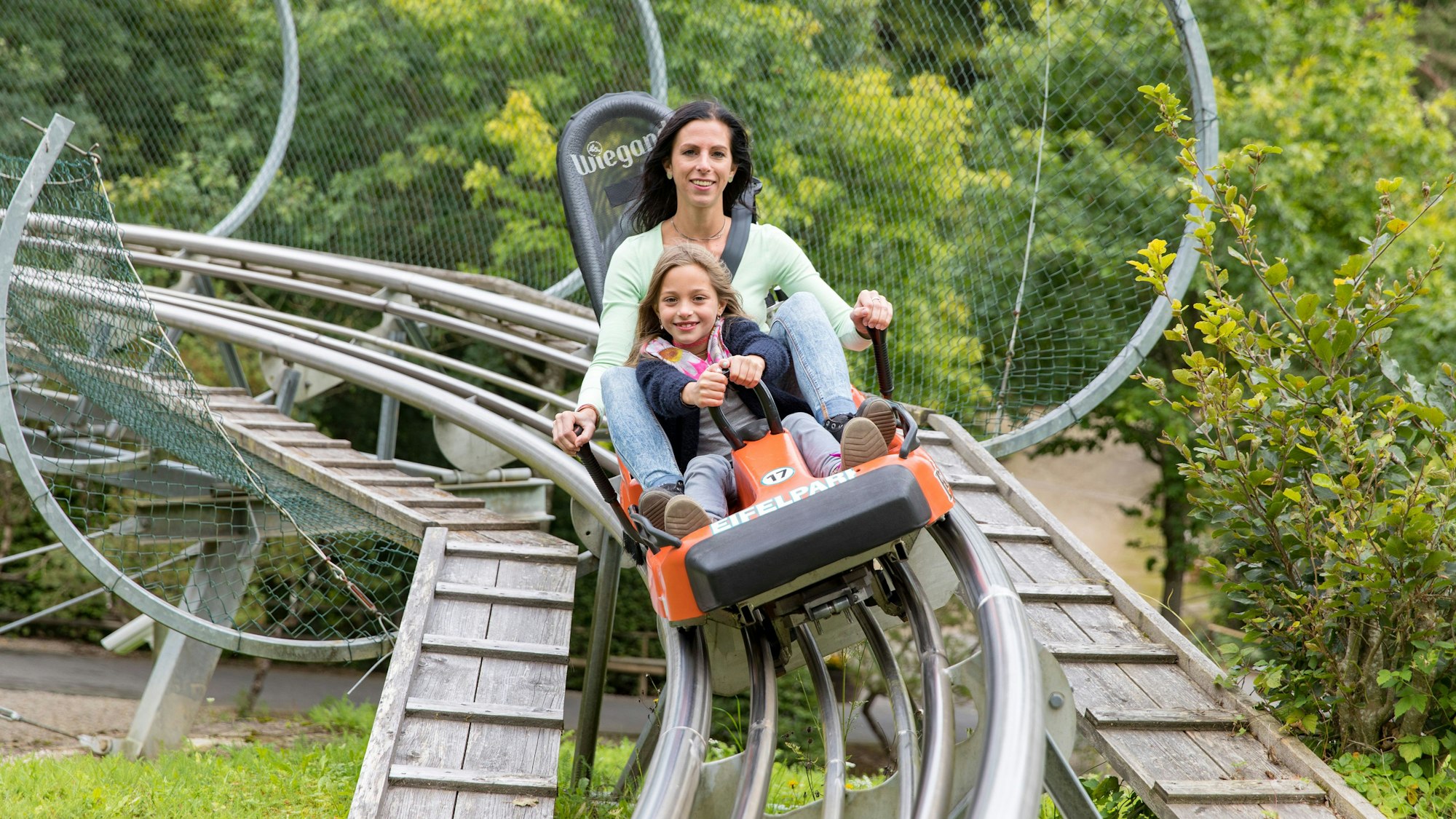 Eine Frau und ein Mädchen fahren in einem Schlitten auf einer Sommerrodelbahn.
