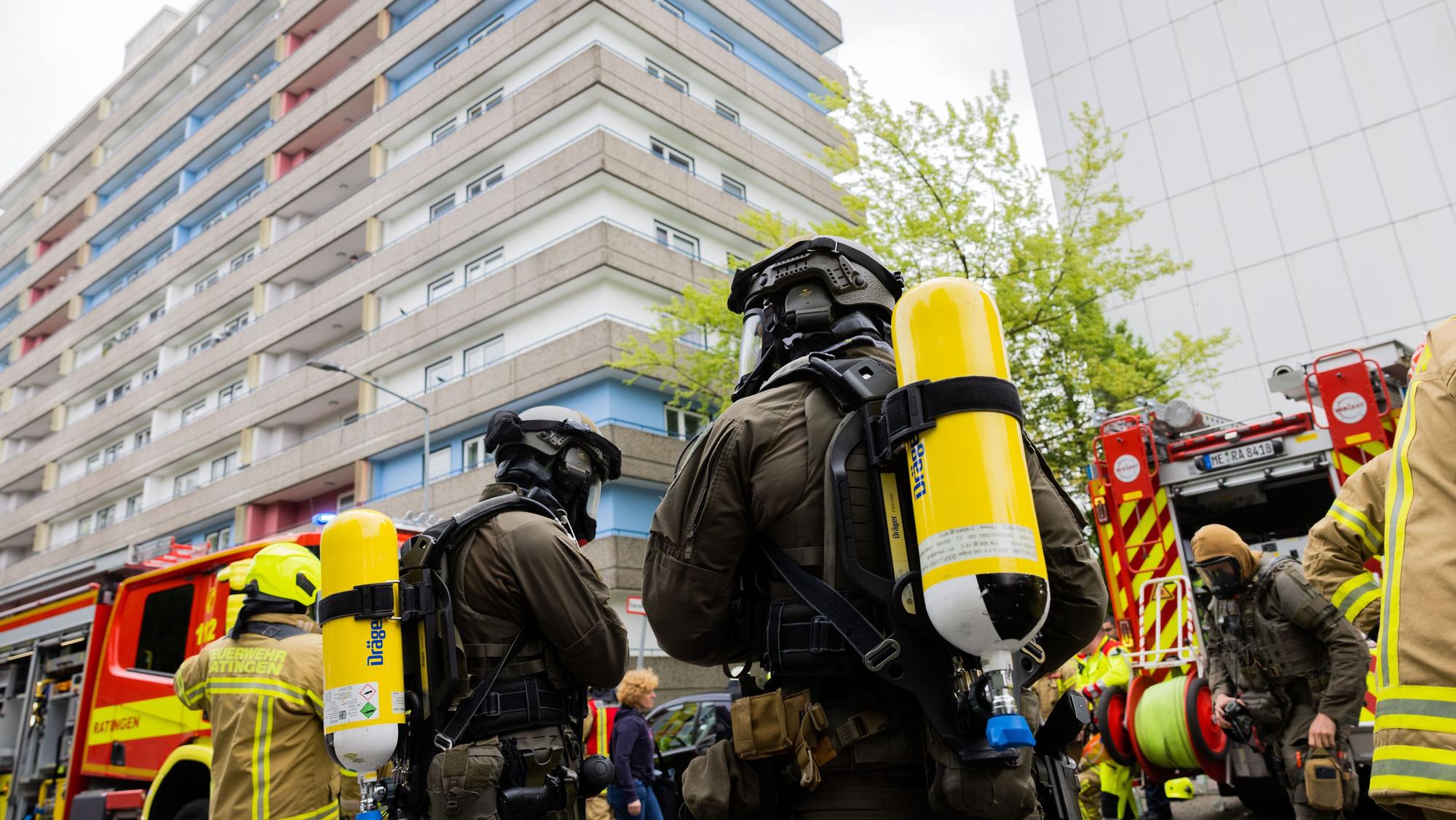 Polizeibeamte mit Gasmasken und Feuerwehrleute stehen während des Einsatzes vor dem Hochhaus in Ratingen.